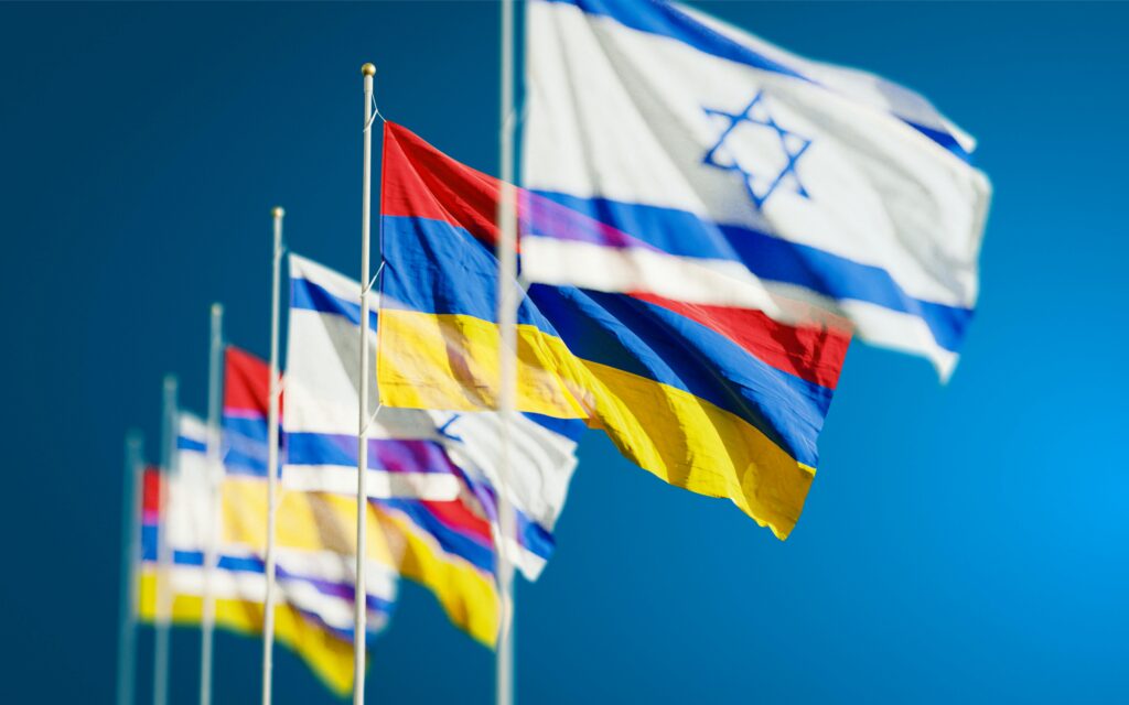 Vibrant national flags of Israel and Armenia waving against a clear blue sky.